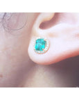 1.55 carat emerald stud earring with halo diamonds, set in 14K yellow gold, worn on an ear.