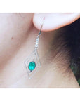 A diamond-shaped earring with a natural marquise emerald worn by a woman.