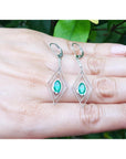 Diamond-shaped earrings with marquise emeralds gemstones placed on fingers against a natural background.