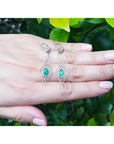 Deep bluish-green emerald marquise earrings in 14K gold with diamond accents, dangling from lever backs.