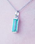 A white gold emerald pendant on a light skin background