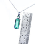 Necklace with a Colombian emerald pendant next to a ruler for scale on a white background