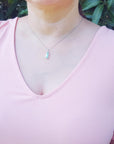 A woman wearing a pink top with a Colombian emerald pendant against a green leafy background.