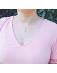 A woman wearing a pink top with a Colombian emerald pendant against a green leafy background.