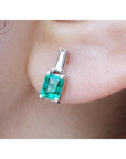 close-up of a Colombian emerald and baguette diamond stud earring on an earlobe.