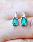 A close-up view of a pair of emerald and baguette diamond earrings placed between fingers.