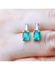 A close-up view of a pair of emerald and baguette diamond earrings placed between fingers.