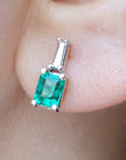 close-up of a Colombian emerald and baguette diamond stud earring on an earlobe.