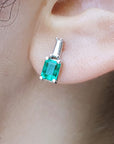 A very close view of a earlobe wearing a natural emerald and baguette diamond earring.