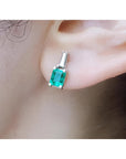 Colombian emerald and baguette diamond stud earrings, 14K white gold, on an ear.