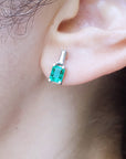 Close up of an ear wearing a Muzo Colombian emerald and baguette diamond earring.