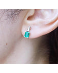 Close up of an ear wearing a Muzo Colombian emerald and baguette diamond earring.