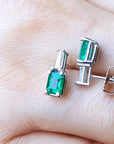 A pair of emerald and baguette diamond earrings front and side profile view placed on fingers.