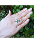 Colombian emerald and baguette diamond stud earrings, 14K gold, on a hand with green leaves.