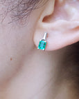 A woman's ear wearing a genuine emerald and baguette diamond earring.