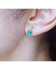 A woman's ear wearing a genuine emerald and baguette diamond earring.
