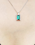 Emerald gemstone pendant on a white gold chain against a beige skin background.
