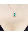 14K white gold baguette cut emerald and diamond pendant necklace on a woman's chest.