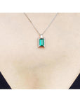 14K white gold baguette cut emerald and diamond pendant necklace on a woman's chest.
