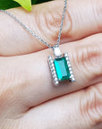Baguette cut emerald gemstone pendant on a white gold chain held between fingers.