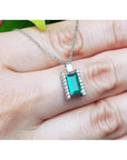 14K white gold emerald and diamond baguette cut pendant necklace on a hand.