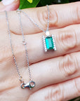 White gold necklace with a natural emerald gemstone pendant on a hand against a natural background.