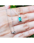 White gold necklace with a natural emerald gemstone pendant on a hand against a natural background.