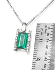 Emerald and diamond baguette pendant on a chain with a ruler for scale on a white background.