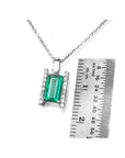 Emerald and diamond baguette pendant on a chain with a ruler for scale on a white background.