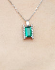 Emerald gemstone pendant on a white gold chain against a beige skin background.