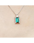 Emerald gemstone pendant on a white gold chain against a beige skin background.