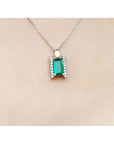 Emerald gemstone pendant on a white gold chain against a beige skin background.