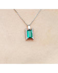 Emerald gemstone pendant on a white gold chain against a beige skin background.