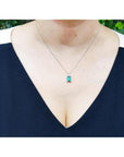 Baguette cut emerald and diamond pendant necklace in 14K white gold, worn on a woman's chest.