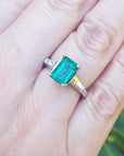 Emerald ring on a hand with a blurred green background.