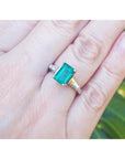 Emerald ring on a hand with a blurred green background.