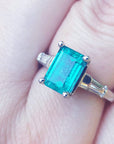 A three stone emerald and baguette side diamond ring in white gold on a finger.