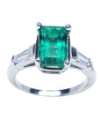 A 18k white gold three stone emerald and baguette side diamond ring on a top view and side profile position.