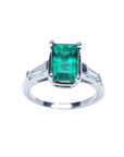 A 18k white gold three stone emerald and baguette side diamond ring on a top view and side profile position.