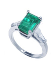 This 18k white gold emerald ring with side baguette diamonds is on a tilted position displaying a top view and side profile.