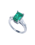 This 18k white gold emerald ring with side baguette diamonds is on a tilted position displaying a top view and side profile.