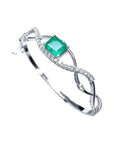 14K white gold bangle with a central emerald-cut emerald and entwined diamond strips.