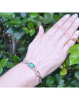 Emerald-cut emerald and natural diamond bangle bracelet in 14K white gold on a woman's wrist.