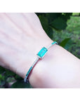 Emerald-cut Colombian emerald bangle bracelet with natural diamonds in 14K white gold on a wrist.