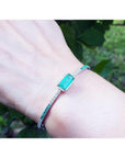 Emerald-cut Colombian emerald bangle bracelet with natural diamonds in 14K white gold on a wrist.