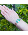 14K yellow gold bangle with round Colombian emeralds and diamonds in a floral design on a hand.