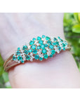 An emerald bangle bracelet round cut Colombian emeralds and natural diamonds in 14k yellow gold on a wrist.