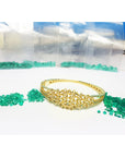 Gold bracelet with natural loose emeralds on a white surface.