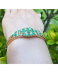 14K yellow gold bangle with round Colombian emeralds and diamonds in a floral design.
