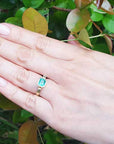 Hand wearing a colombian emerald solitaire ring bezel set against a green leafy background